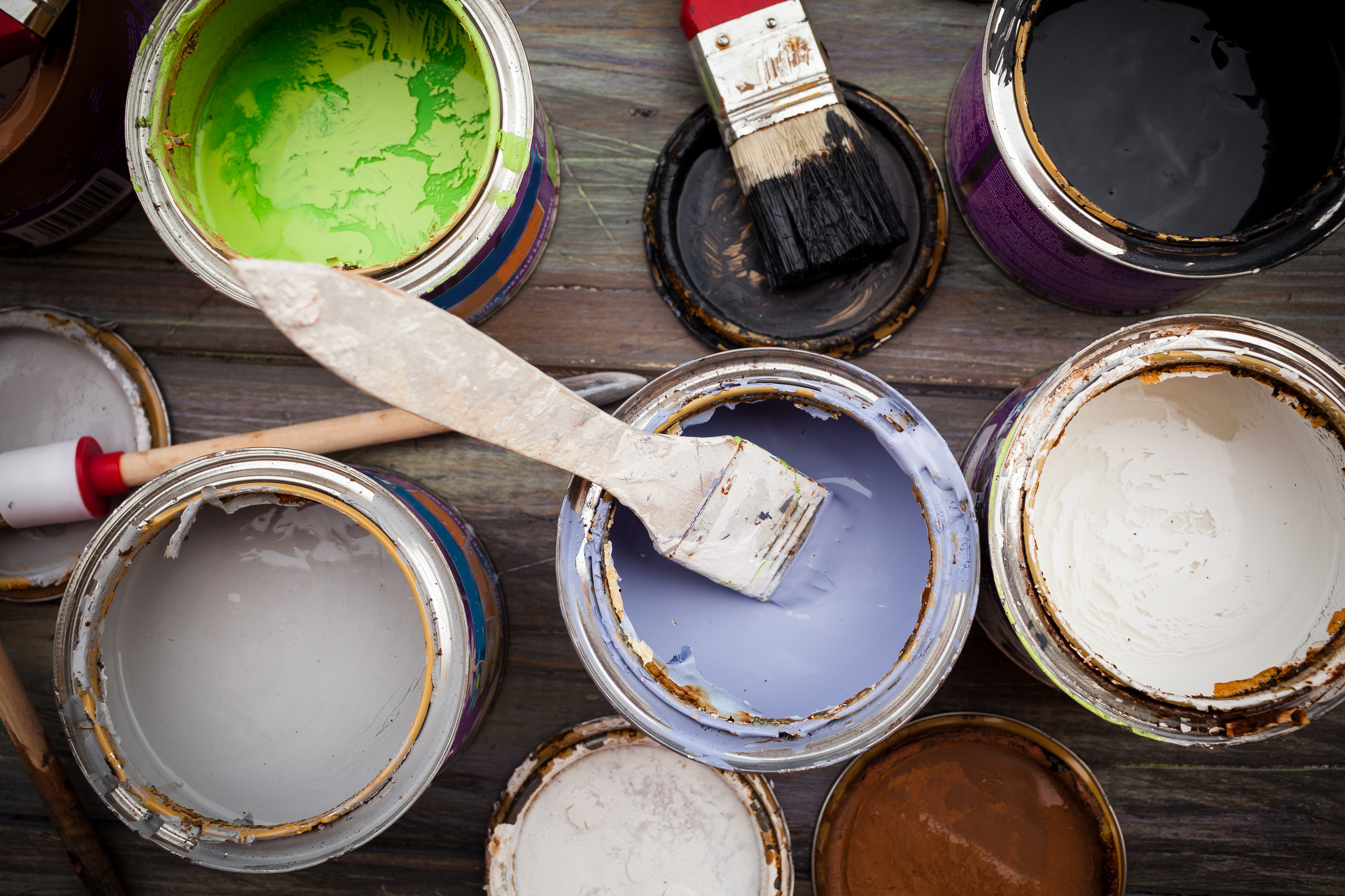 Many colorful cans of paint open with paintbrushes sitting in them. Picture from above.