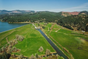 An aerial view of where water is released from Scoggins Dam. Part of Hagg Lake is visible on the left, with trees and hills in the background.