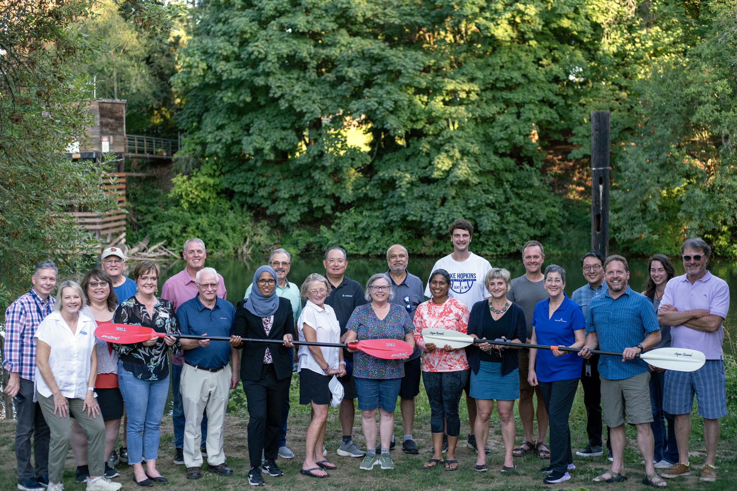 Members of CWAC, the CWS Board, and CWS staff , some holding kayak paddles, stand in two rows by the Tualatin River.