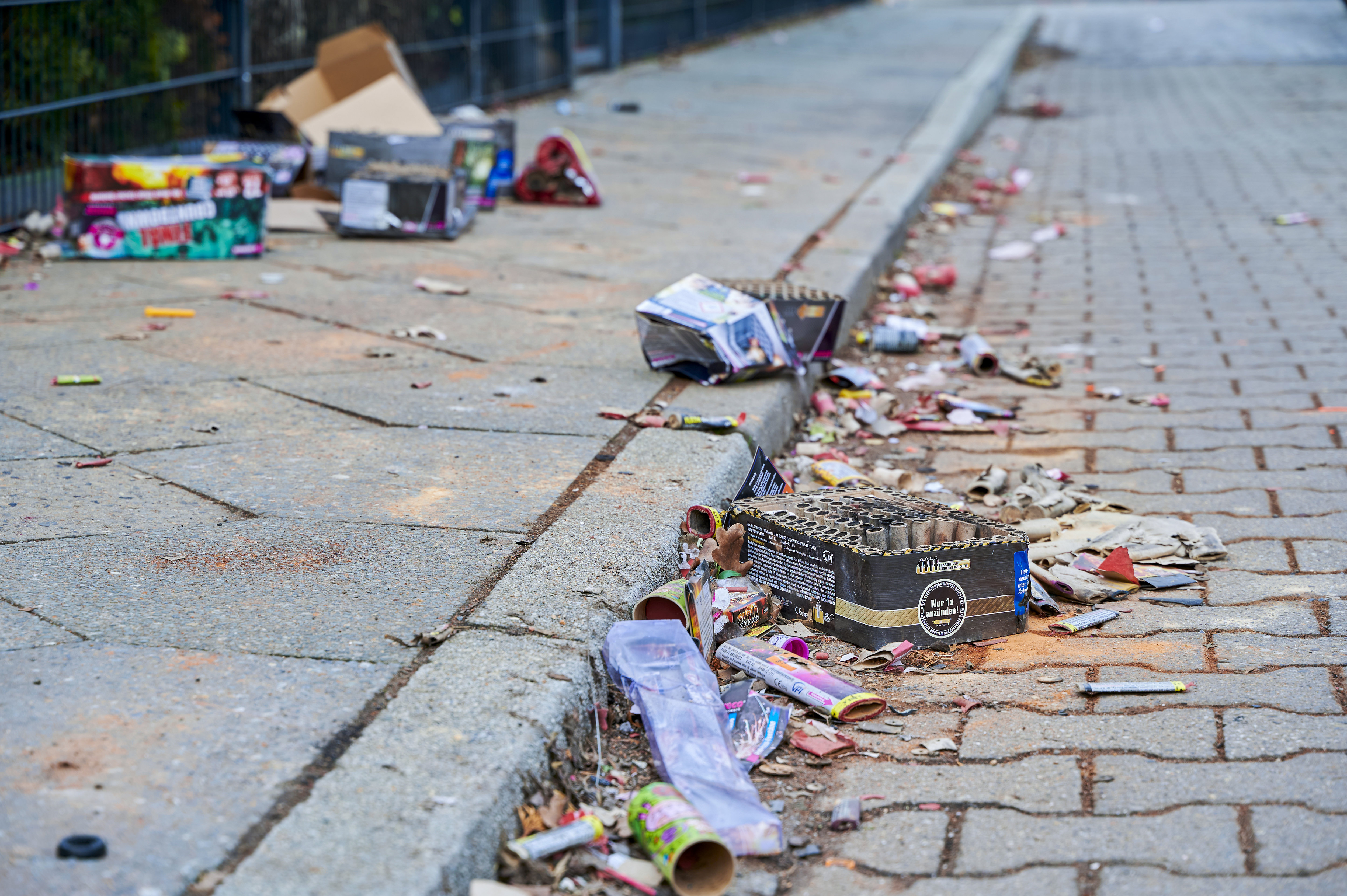 Spent fireworks collect in a debris pile along the curb of a sidewalk.